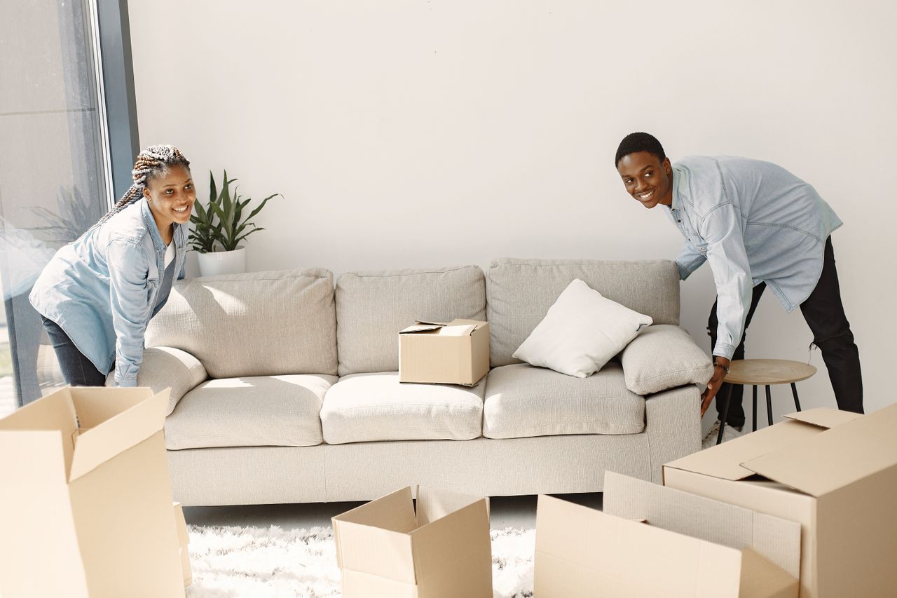 Mastering the First Impression: Your intriguing post title goes here A cheerful couple moving furniture in a well-lit modern living room with cardboard boxes.