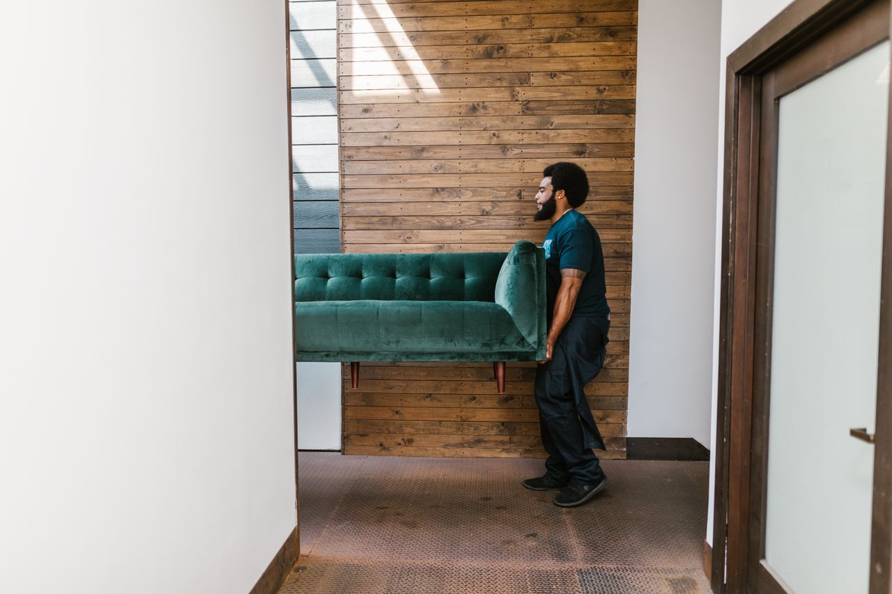The Art of Drawing Readers In: Your attractive post title goes here A mover carries a green sofa indoors, showcasing modern interior design and relocation services.